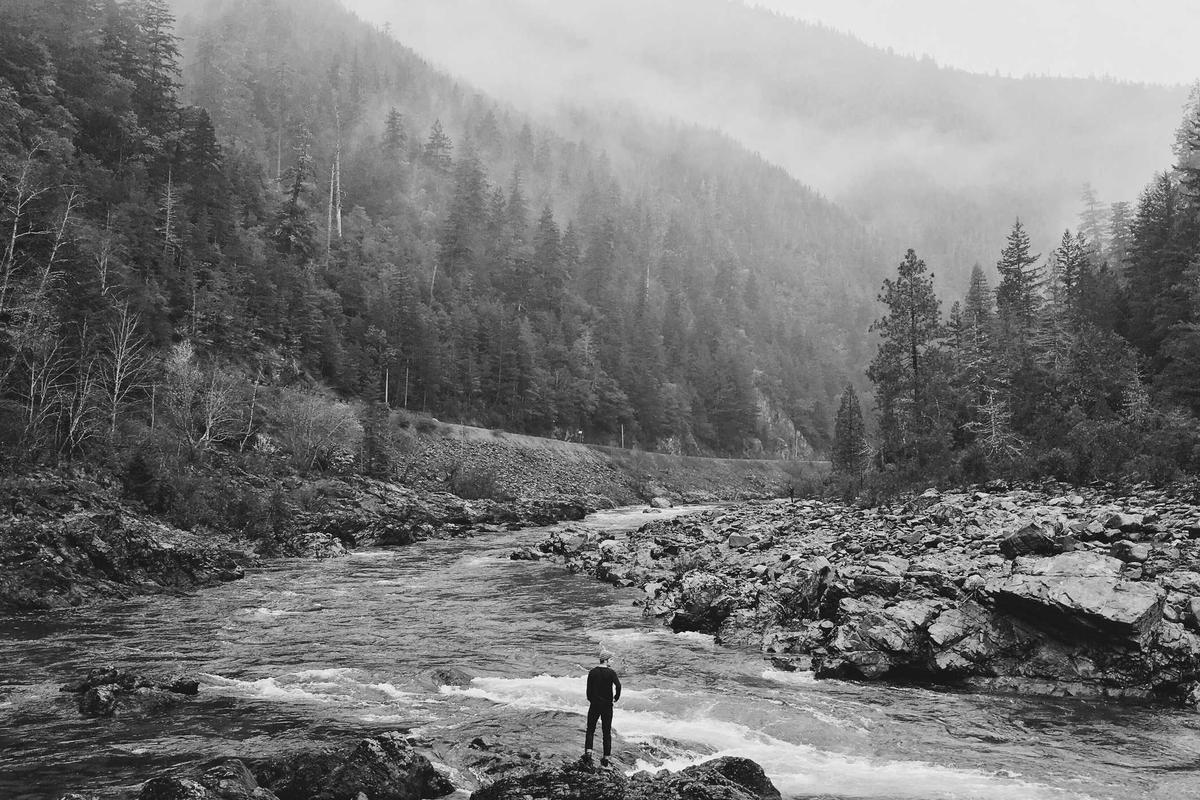A lone figure on a riverbank beneath forested hills